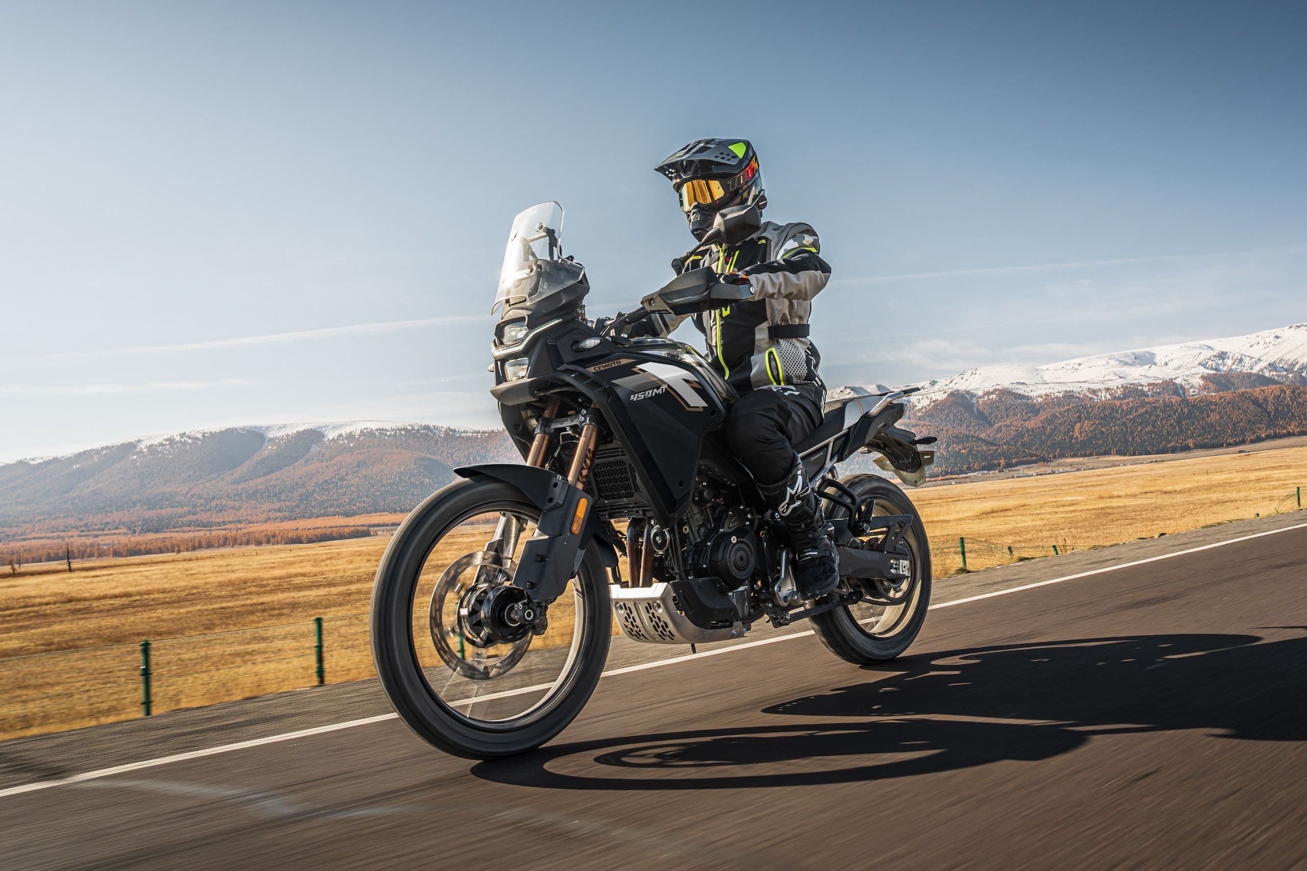 Rider on a black adventure motorcycle driving on an asphalt road through mountains.