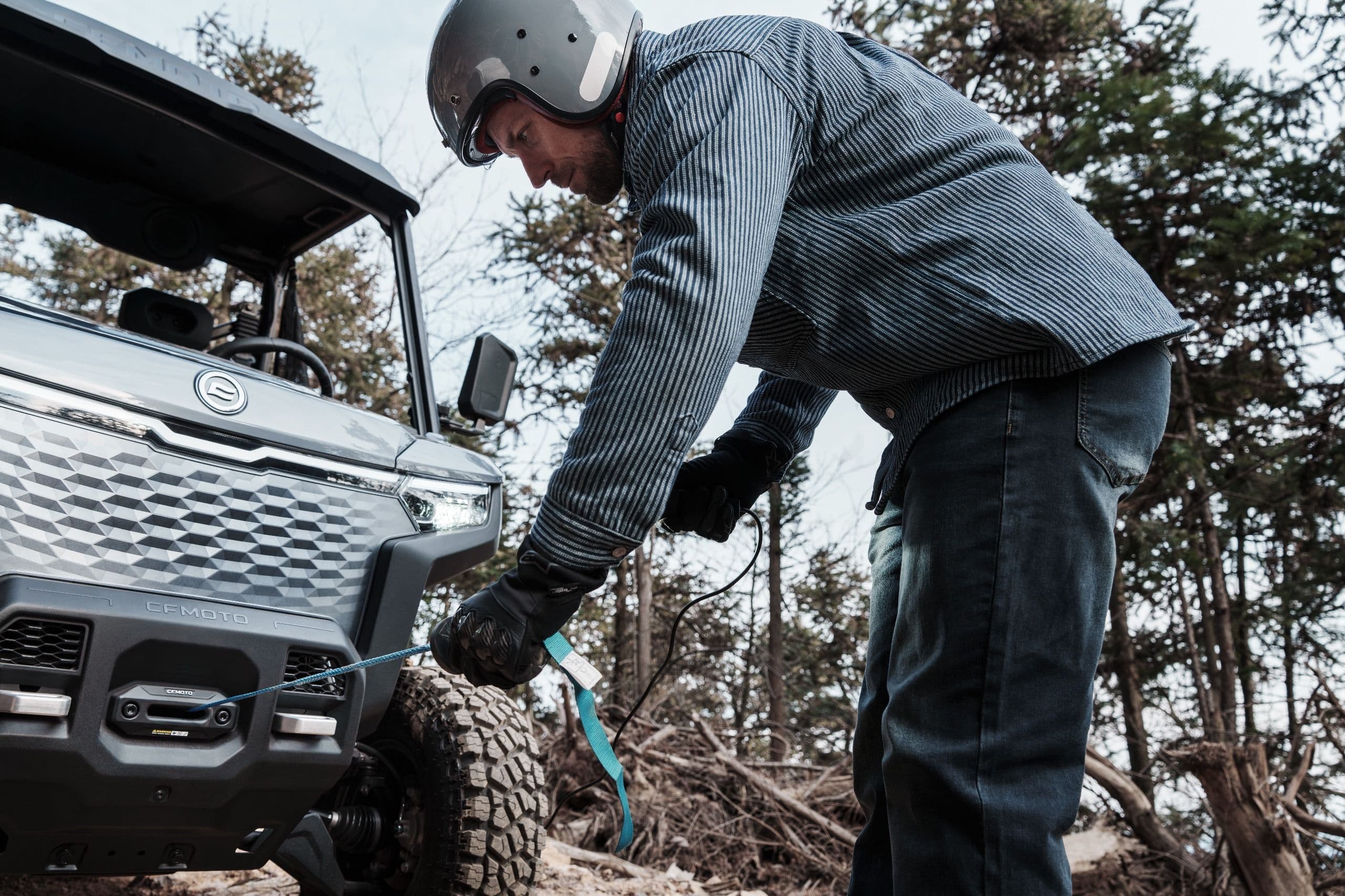 Man in helmet connecting a winch cable to the front bumper of a UTV.